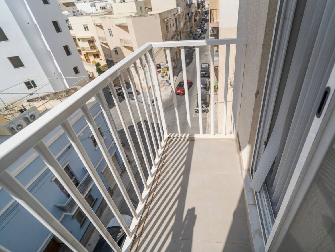 Un balcón con barandas blancas que da a una calle con coches y edificios.