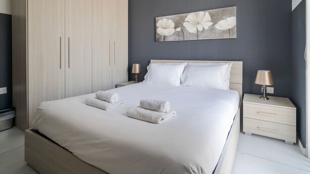 A modern bedroom with a large bed, two bedside tables, a wardrobe, and a floral artwork on the wall. - Cosy 1BR fully equipped Apt with balcony w/WIFI ! (Gżira)