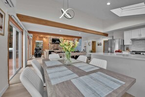 A modern kitchen with white cabinets, a central island, and a dining area with a wooden table and white chairs. - Lakefront | Sauna | Pool Table | Firepit | Refined (Tobyhanna)