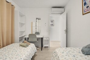 A bedroom with two beds, a desk, a chair, and a wardrobe.