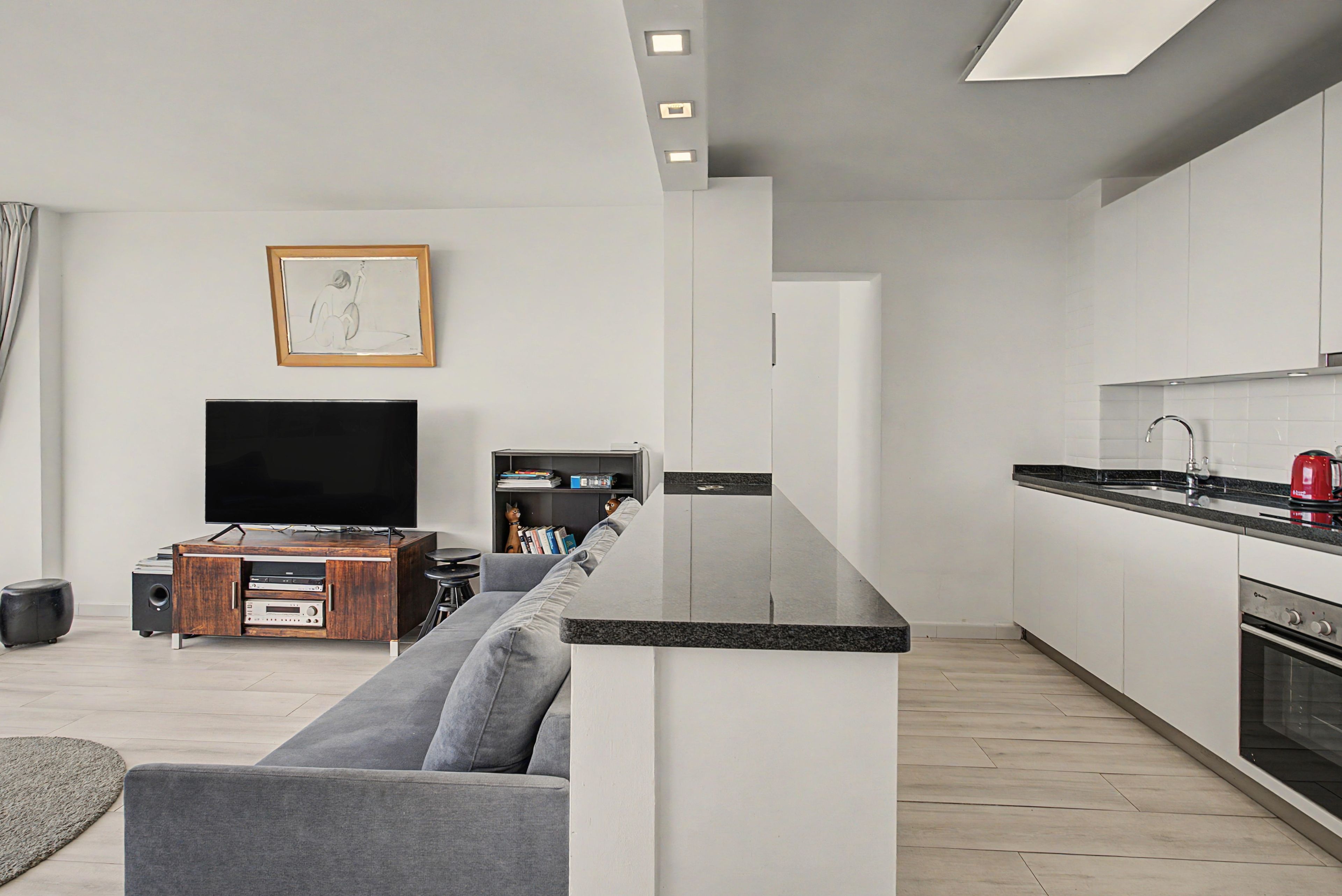 A modern living room with a grey sofa, a flat-screen TV, and a wooden entertainment unit.