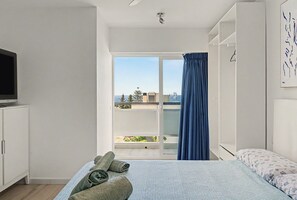 A hotel room with a bed, a television, a balcony with a view, and a window with curtains.