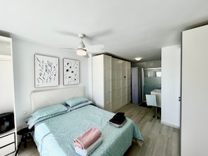 A bedroom with a bed, a ceiling fan, a wardrobe, and a bathroom visible through an open door.