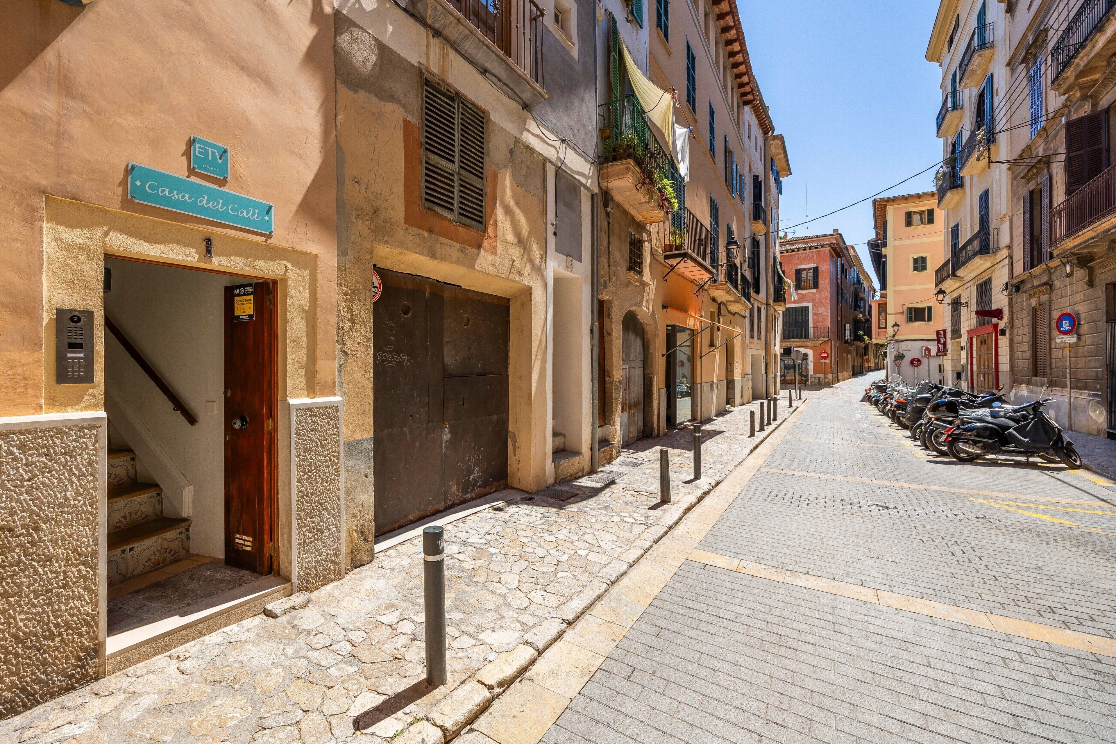 Una calle estrecha con un edificio que dice 'Casa del Catt' y una fila de motocicletas estacionadas.
