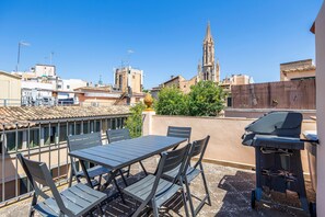 A rooftop terrace with a table and chairs, a barbecue grill, and a view of a church tower. - Spectacular rooftop with cathedral views and BBQ (Palma)