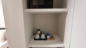 Una kitchenette compacta con microondas, cafetera y refrigerador pequeño.
