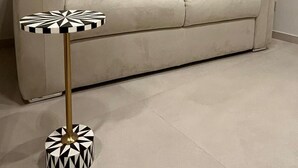 Un sofá beige frente a una pared lisa, con una lámpara de pie redonda, de estilo pequeño y con estampado blanco y negro, y una base dorada.