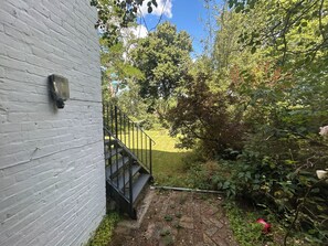 A brick wall with a light fixture, a staircase leading to a grassy area, and dense foliage.