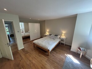 A bedroom with a wooden floor, a bed with white bedding, two bedside tables with lamps, and a wardrobe with mirrors.