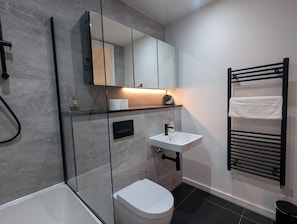 A modern bathroom with a glass shower enclosure, a white toilet, a sink with a faucet, and a towel rack.