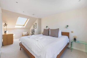 A bedroom with a skylight, a bed with pillows, a bedside table with a lamp, and a chair.