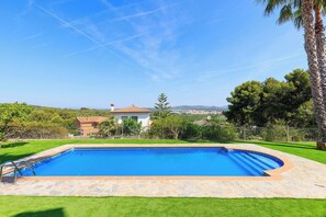 A swimming pool with a stone border, a house in the background, and a clear sky. - Mediterranean Pool Villa - Unik Vacation (La Riera de Gaià)