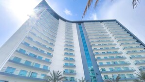 A high-rise hotel with multiple balconies, a central blue vertical feature, and palm trees in the foreground. - Urban Escape Studio Pool, Gym & Stylish Living (Dubai)