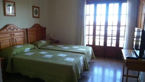A room with two beds, a desk, and a window with blinds. - Hotel Luz del Guadiana (Ayamonte)