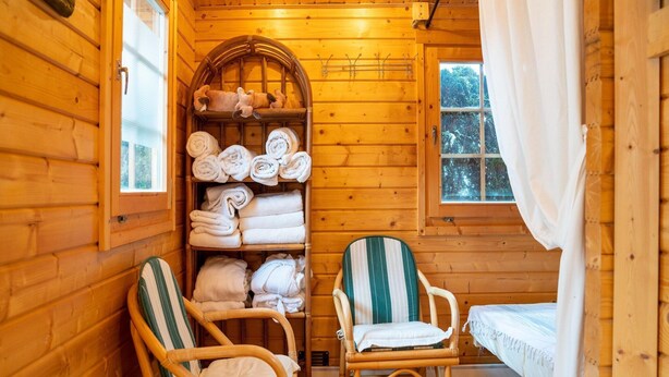 Une chambre confortable dans un chalet, avec des murs en bois, un lit, deux fauteuils en osier et une étagère où sont soigneusement pliées des serviettes.