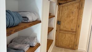 A hallway with wooden shelves holding towels, a wooden door, and a tiled floor. - Roof top MARZE (Aubenas)