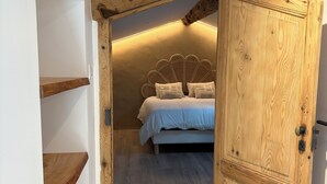 A bedroom with a wooden ceiling, a bed with white bedding, and a wooden door. - Roof top MARZE (Aubenas)