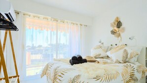 A bedroom with a bed featuring a leaf pattern, a window with sheer curtains, a wooden ladder, and a wall-mounted lamp. - Cosy apartment in Vence with swimming pool & parking (Vence)