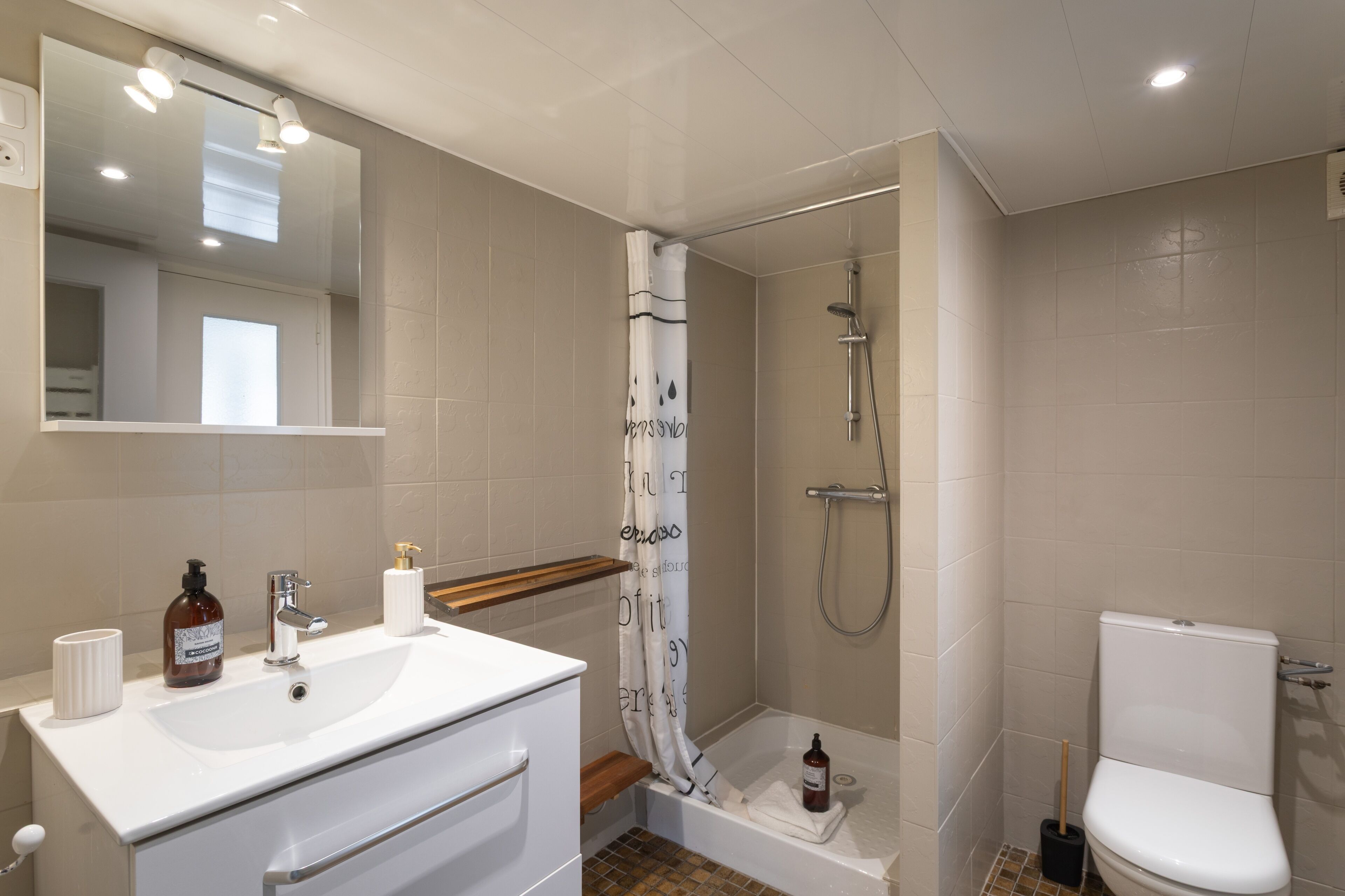 Une salle de bain avec un lavabo blanc, un miroir, une douche et des toilettes.