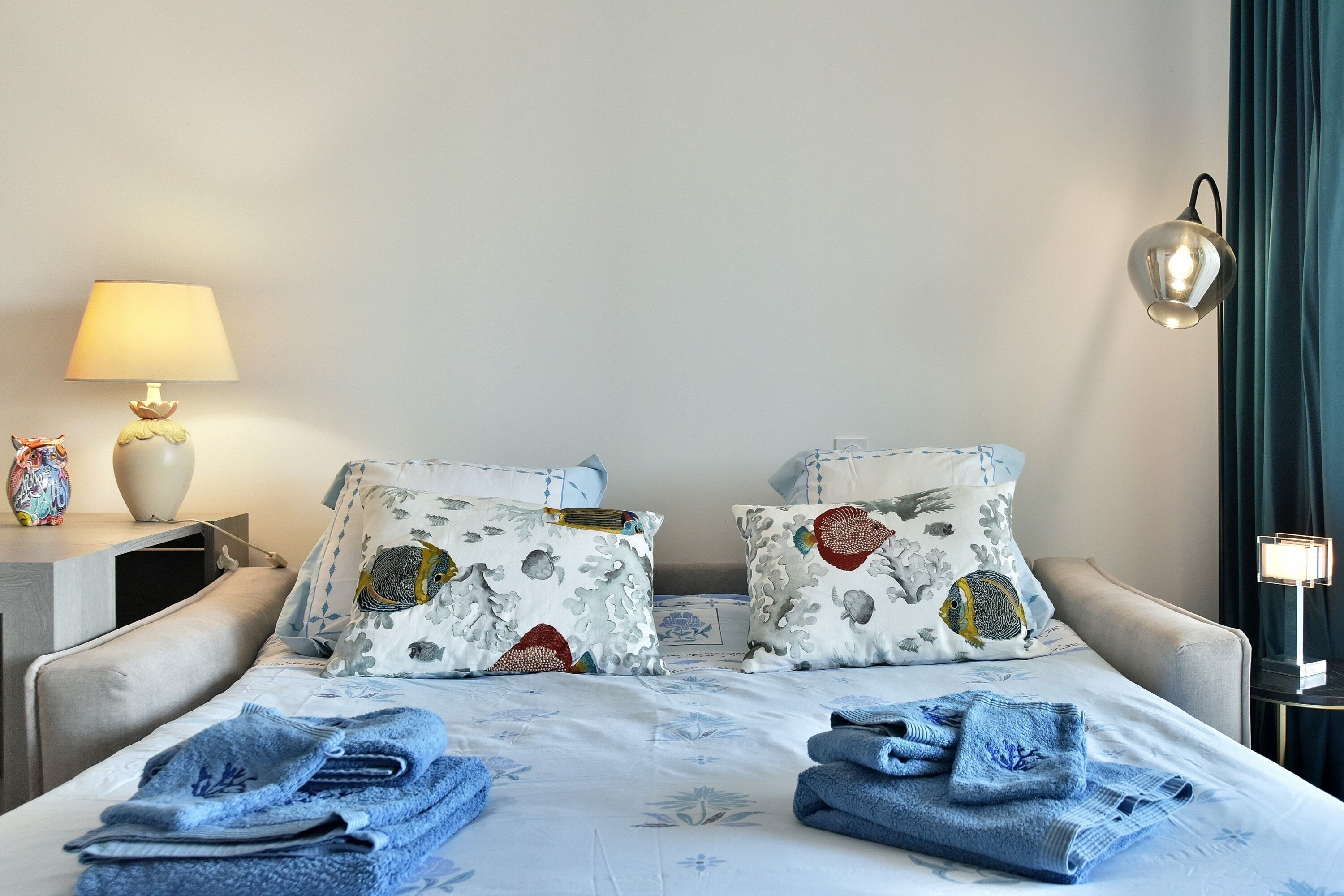 Une chambre d’hôtel avec un lit, deux oreillers à motifs de poissons, une lampe de chevet, une table de chevet et des serviettes pliées.