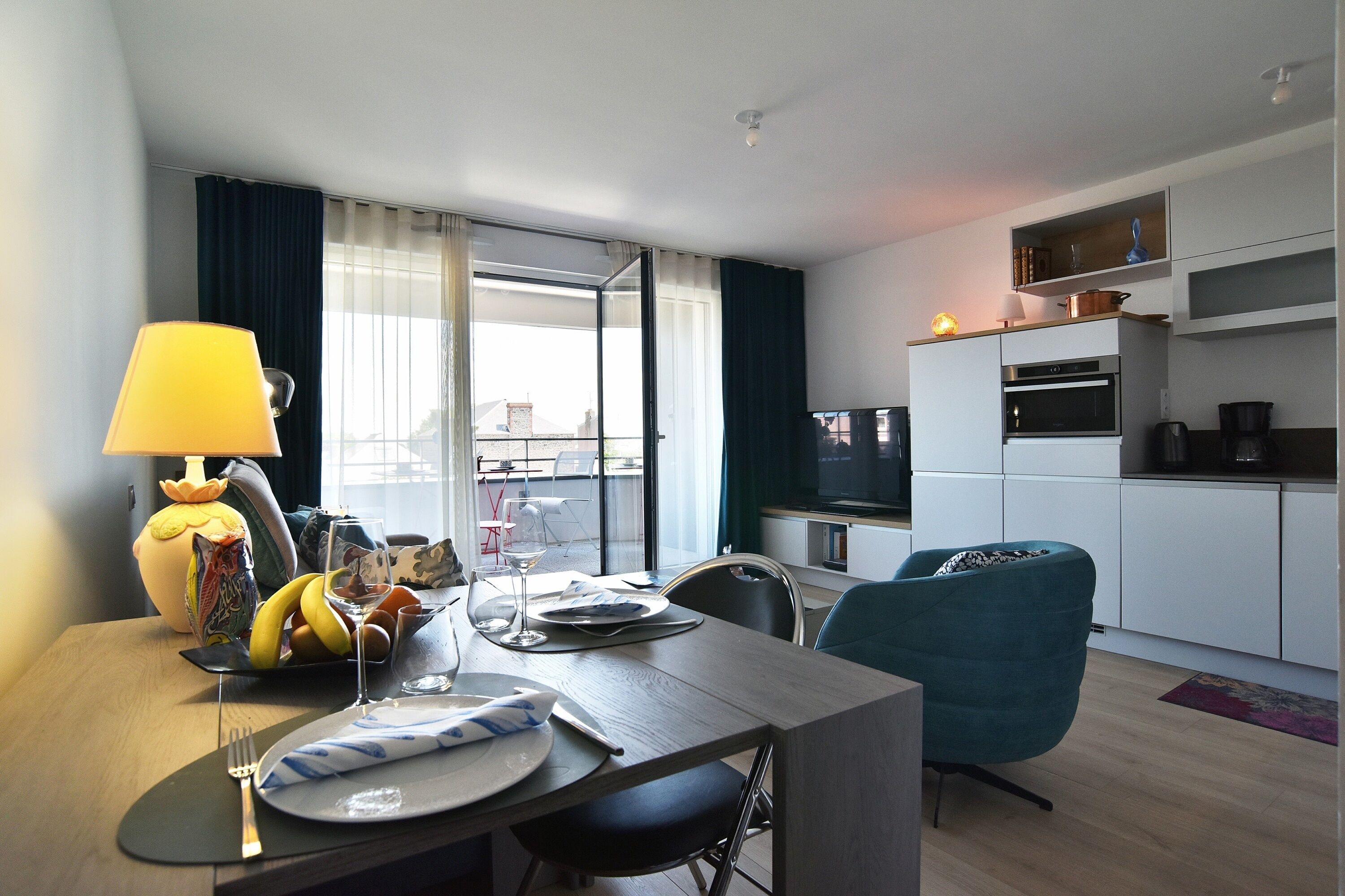 Ein modernes Wohnzimmer mit Essbereich, einer Couch, einem Fernseher und einer Küchenzeile mit Mikrowelle und Backofen.
