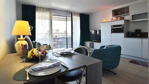 A modern living room with a dining area, a sofa, a TV, and a kitchen area with a microwave and oven. - Horizon Dinardais - Proche Plages (Dinard)