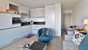 A modern kitchen with white cabinets, a built-in oven, and a dining area with a table set for two. - Horizon Dinardais - Proche Plages (Dinard)