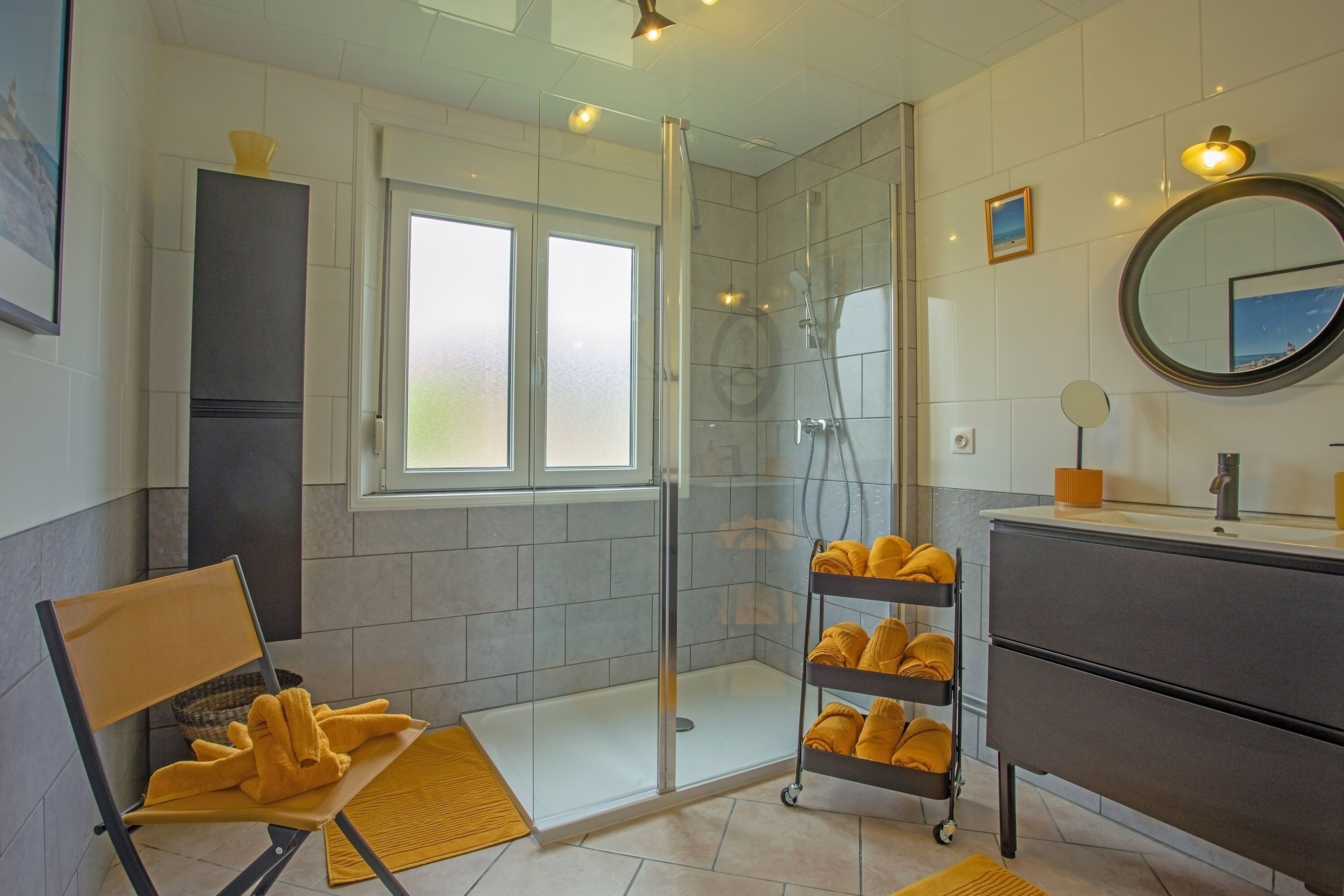 Een moderne badkamer met een douchecabine van glas, een wastafelmeubel met spiegel en een handdoekrek met gele handdoeken.