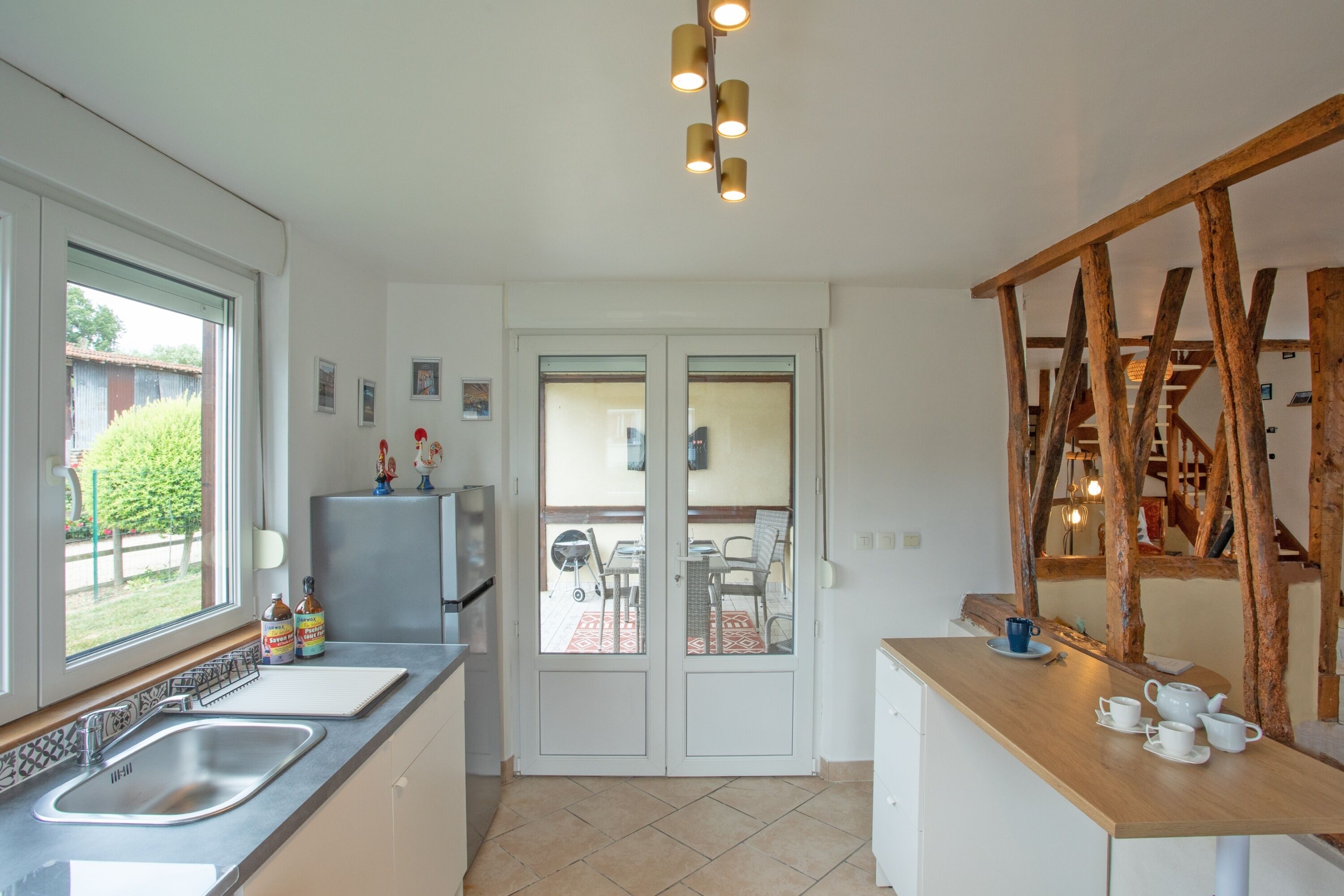 Une cuisine moderne équipée d’un évier, d’un plan de travail et donnant, par de grandes portes vitrées, sur un patio extérieur.