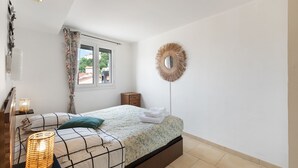 Un dormitorio con cama, lámparas de noche, una ventana, un espejo y un accesorio de iluminación en la pared.