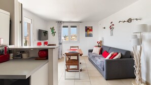 Una sala moderna con un sofá gris, cojines rojos, una mesa de comedor de madera y un televisor montado en la pared.