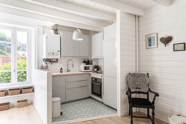 A compact kitchen with white cabinets, a microwave, and a coffee maker. There is a window with a view of greenery outside.