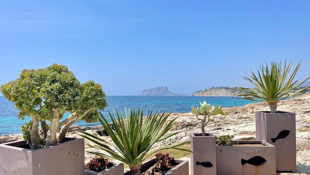 A coastal landscape with a rocky beach, a clear blue sky, and a distant island.