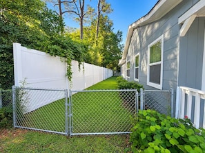 A residential property with a fenced yard, a white fence, and a house with a grey exterior. - Perfect Two Bedrooms with Fenced Yard and Three Blocks to Beach (Myrtle Beach)