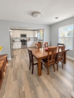 A modern kitchen with white cabinets, stainless steel appliances, and a dining area with a wooden table and chairs. - Perfect Two Bedrooms with Fenced Yard and Three Blocks to Beach (Myrtle Beach)