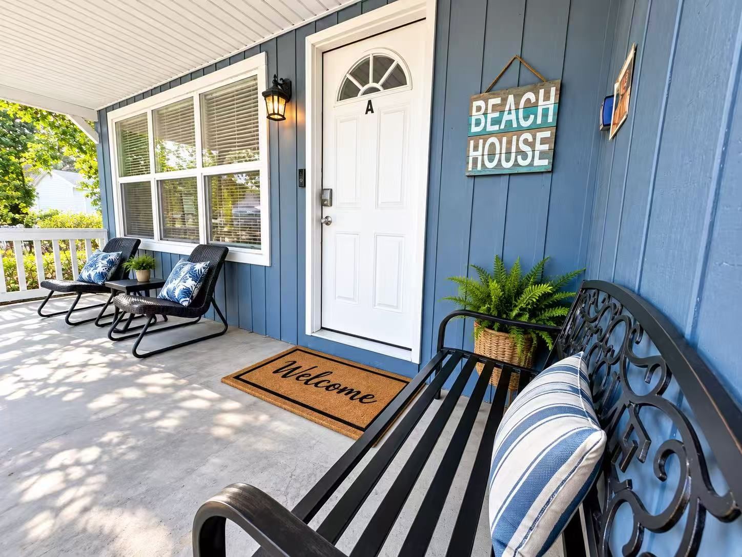 A porch with a bench, two rocking chairs, a welcome mat, and a sign that reads 'BEACH HOUSE.'