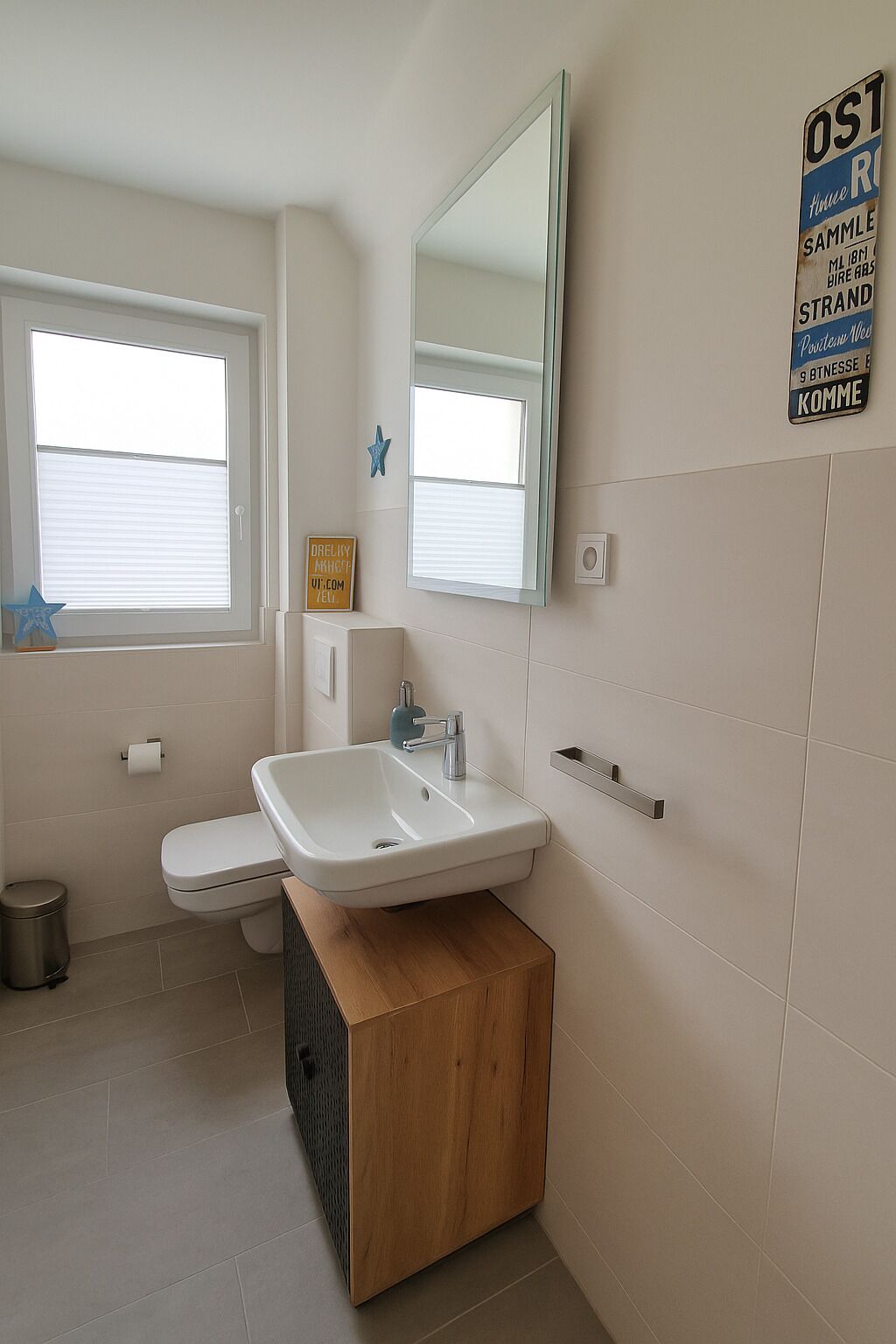 Um banheiro moderno com pia branca, um espelho e um vaso sanitário. Há uma decoração em forma de estrela na parede e uma placa com texto.