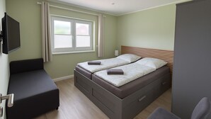 A bedroom with a bed, a small desk, a chair, a TV, and a window with curtains.
