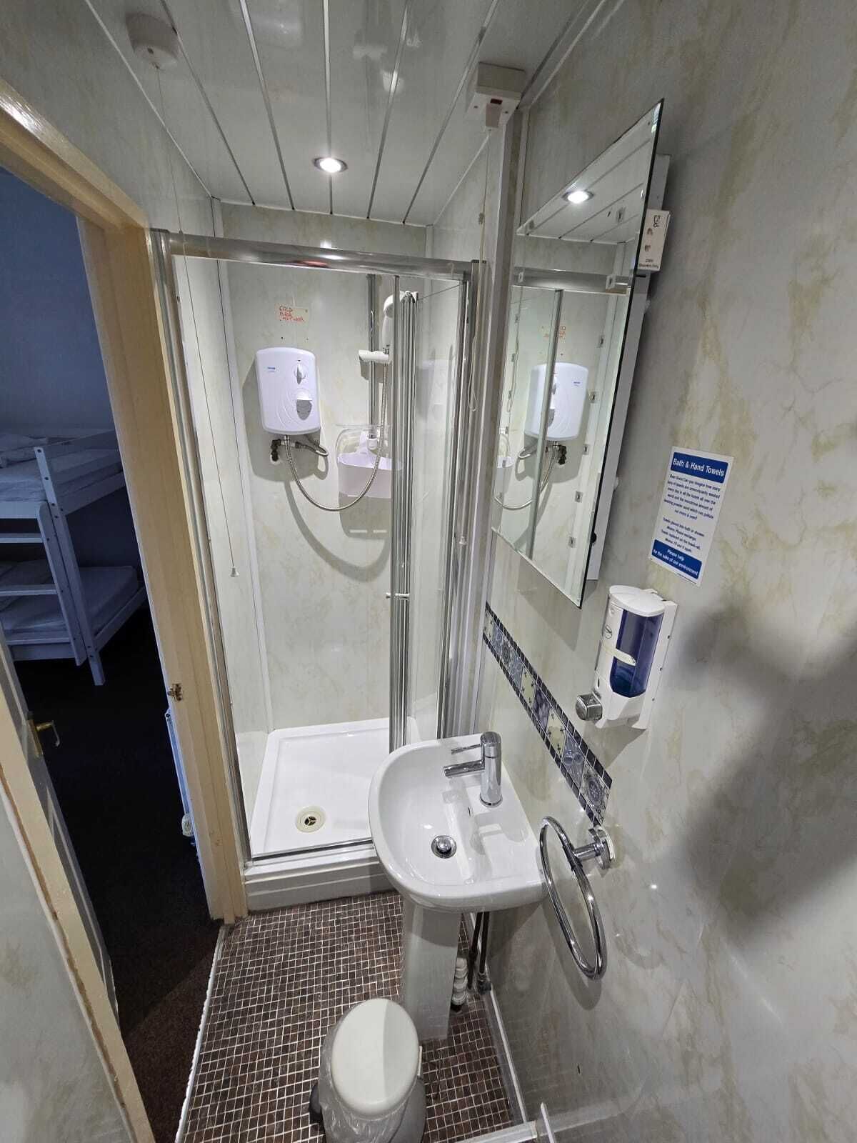 A bathroom with a glass-enclosed shower, a sink, a toilet, and a hand dryer.