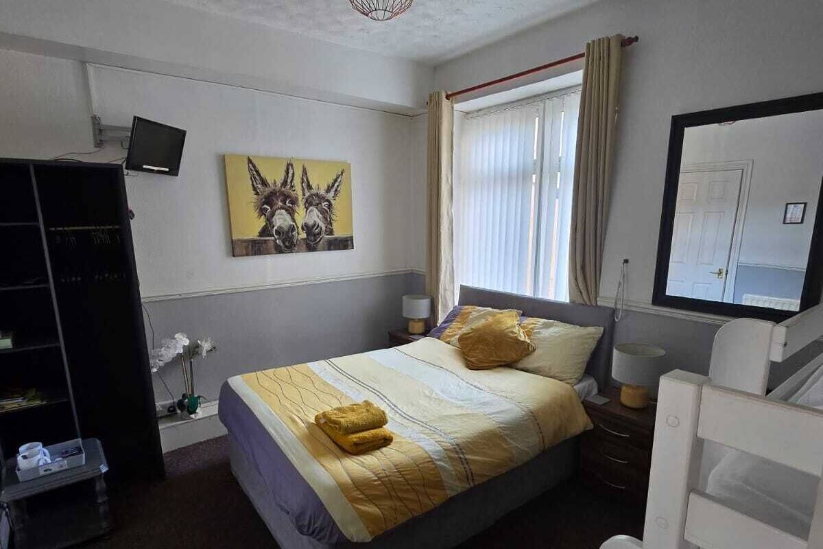 A bedroom with a bed, a desk, a chair, a TV, and a painting of horses.