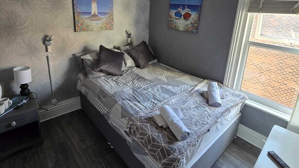 A bedroom with a large bed, a nightstand, a lamp, and two paintings on the wall.