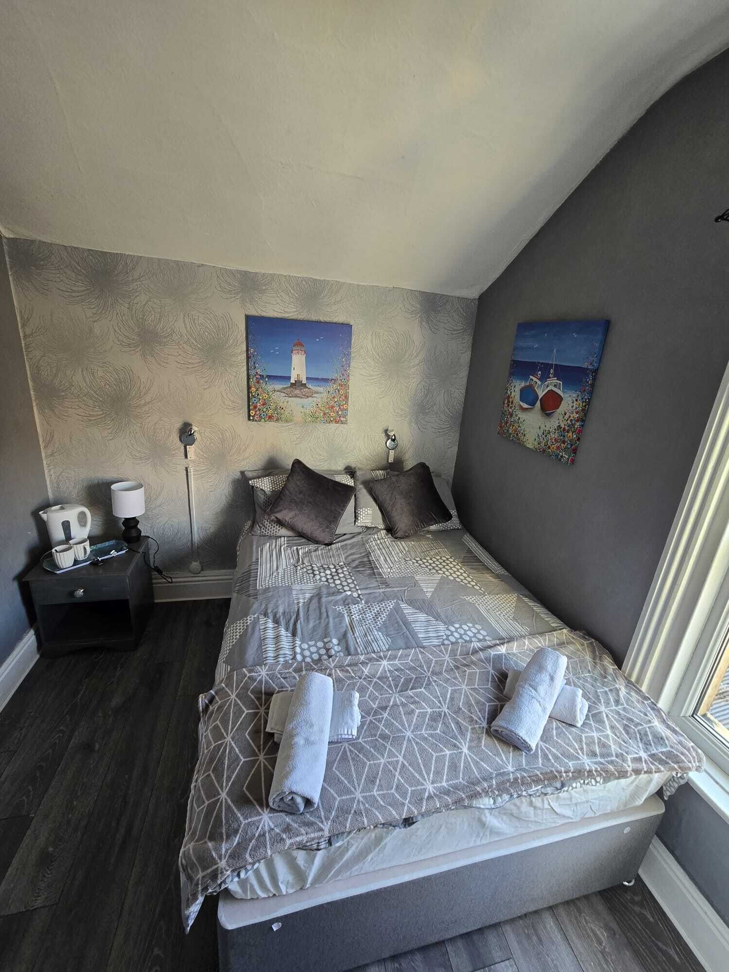 Une chambre à coucher avec un grand lit, deux tableaux accrochés aux murs, une table de chevet avec une lampe et une fenêtre.