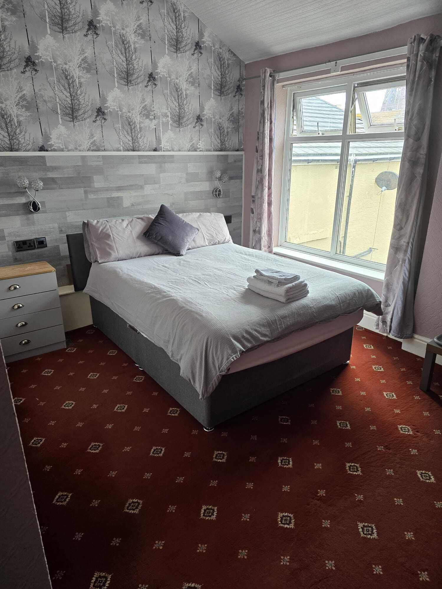 A bedroom with a bed, a nightstand, a dresser, and a window with curtains.