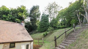 A rustic house with a sloped roof, a wooden staircase, and a grassy hill in the background.