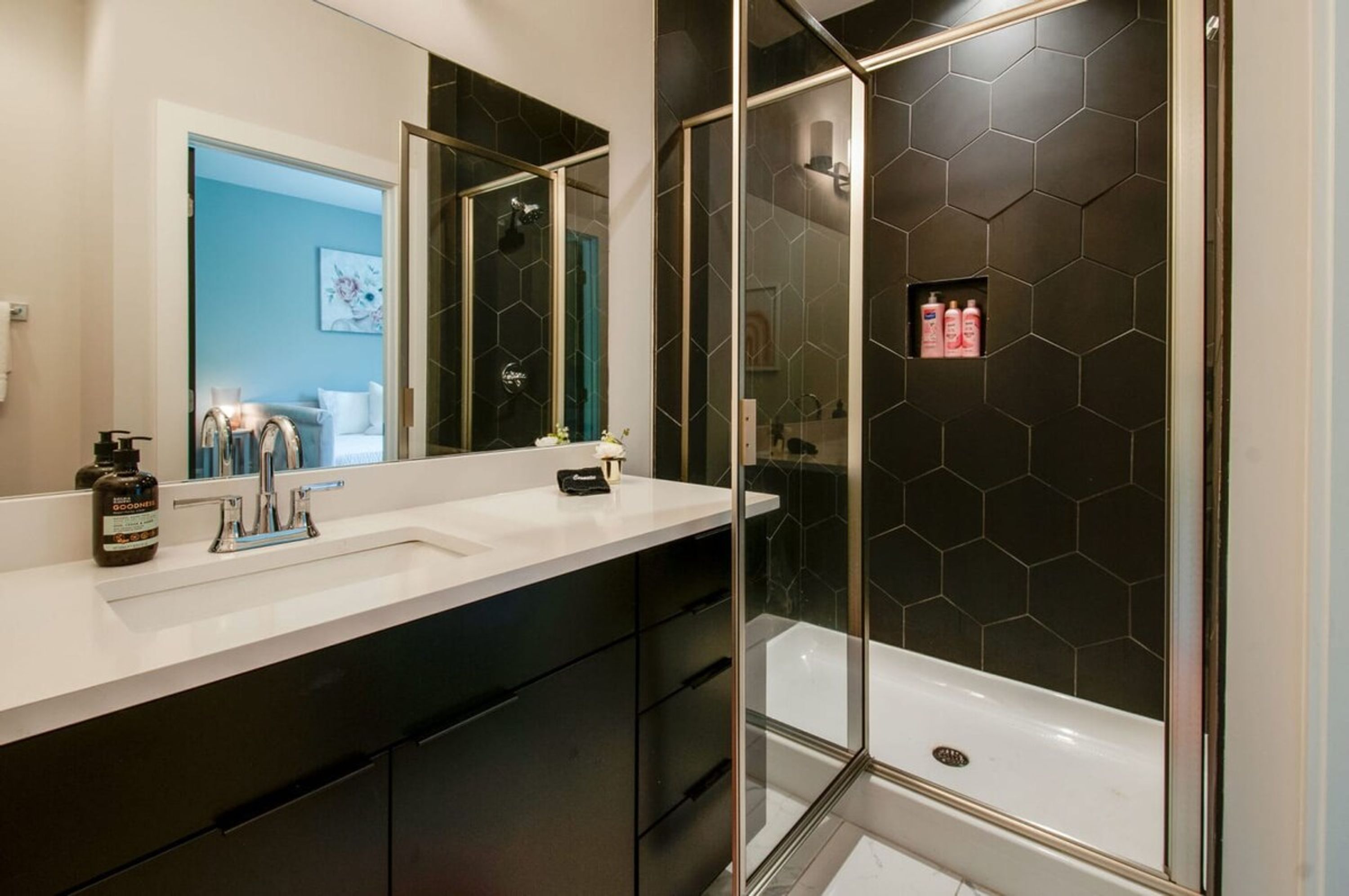 A modern bathroom with a white sink, black cabinets, a glass-enclosed shower, and a hexagonal tile backsplash.