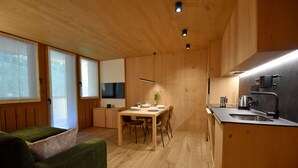 Cocina compacta y moderna con muebles de madera, comedor con una mesa para dos, y una pequeña sala de estar con sofá verde.