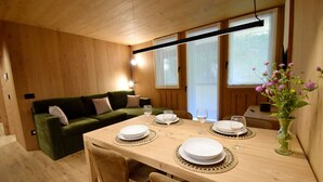 Un interior de madera con una mesa de comedor dispuesta para cuatro personas, un sofá verde y un florero con flores.