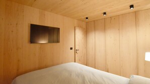 Un dormitorio con paredes de madera, una cama, una puerta y un televisor montado.