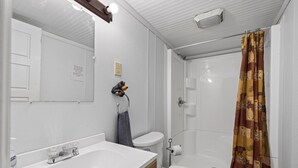 A bathroom with a white sink, toilet, and shower. There is a towel hanging on the wall and a shower curtain with a pattern.