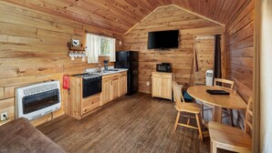 A wooden cabin interior with a kitchen, dining area, and a ceiling fan.